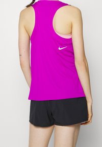Lilla atletisk tank top med racerback-design, med et lille hvidt Nike-logo på ryggen, kombineret med sorte shorts. Glat tekstur.
