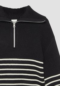 Schwarzer Strickpullover mit hohem Kragen, ausgestattet mit einem Frontreißverschluss und horizontalen weißen Streifen über dem Körper. Texturierte Stoffdetails.