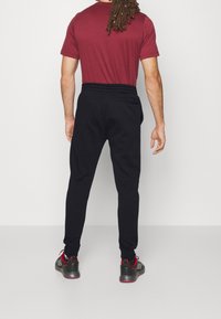 Svarta joggingbyxor med avslappnad passform och elastisk midja, kombinerade med en vinröd t-shirt. Svarta sneakers med röda detaljer fullbordar outfiten.