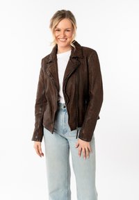 Chaqueta de cuero marrón estilo motero con un patrón de leopardo, que presenta un cuello con muescas y bolsillos con cremallera, combinada con jeans de color azul claro.