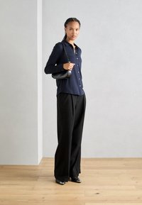Marineblauwe button-up shirt, zwarte wijde broek, zwarte handtas met een schouderband en zwarte puntige schoenen. Casual en gestructureerde outfit.