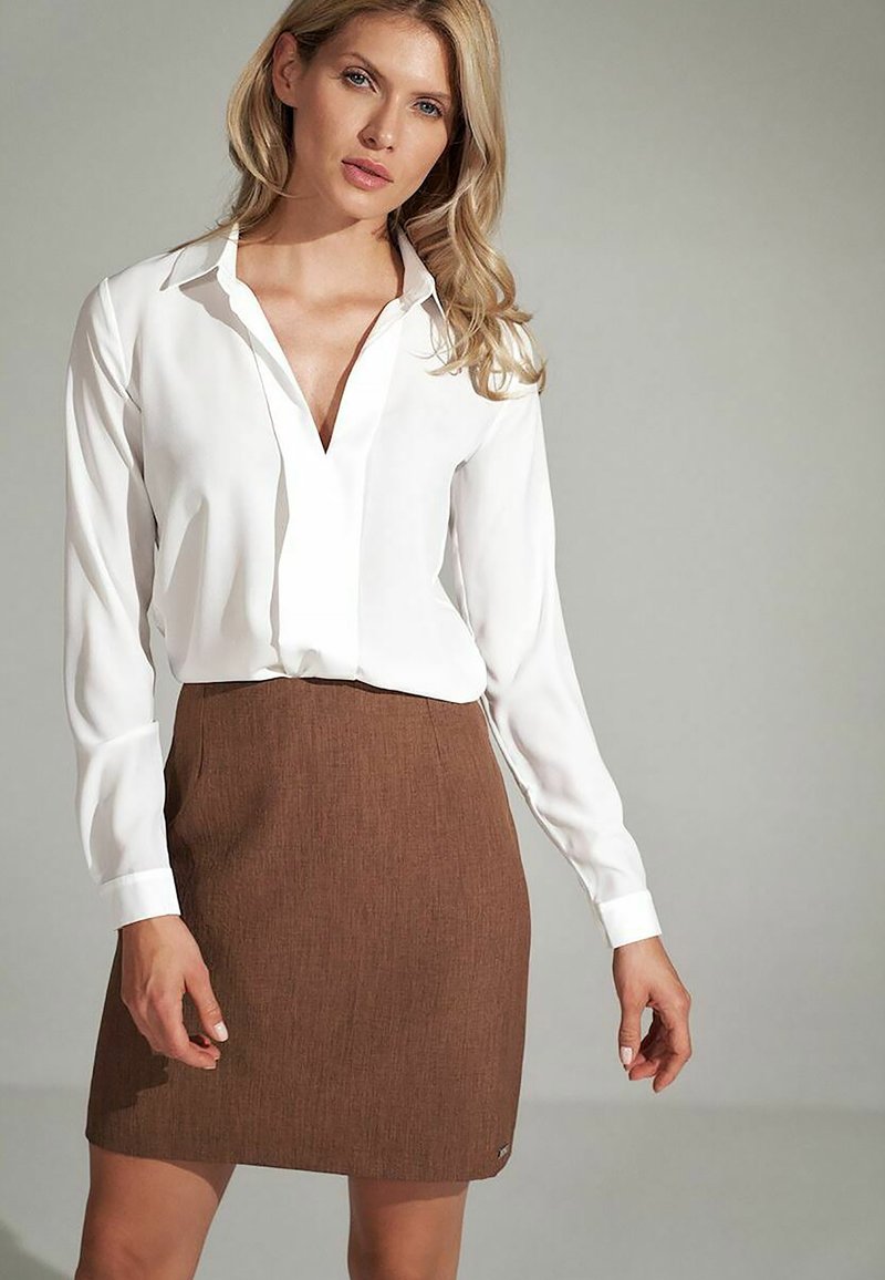 Biała bluzka z długim rękawem i dekoltem w serek, zestawiona z brązową teksturowaną spódnicą. Spódnica ma dopasowany fason i małą metkę z logo u dołu.