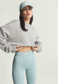 Grå oversize sweatshirt med en liten vit logotyp, kombinerad med ljusblå högmidjade leggings med en vit märkesdetalj på midjebandet.