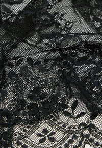 Czarna koronka z misternymi wzorami kwiatowymi, delikatną strukturą siateczkową, subtelnymi falbankami i miękkim, zwiewnym wyglądem.