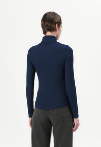 Donkerblauwe geribbelde coltrui met lange mouwen, een aansluitende pasvorm en een zachte textuur, gecombineerd met grijze high-waisted jeans.