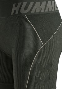 Nahaufnahme von schwarzen, strukturierten Sportleggings mit geripptem Stoff, grauen Nähten, "HUMMEL"-Branding am Bund und Chevron-Logo am Oberschenkel.