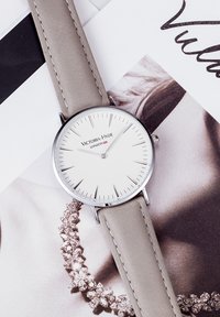 Silberne Armbanduhr mit einem runden weißen Zifferblatt, minimalistischen Stundenmarkierungen und einem hellgrauen Lederarmband mit kontrastierenden Nähten.
