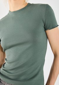 Green ribbed top with short sleeves, crew neck, and frayed edges on sleeves. Made of soft, stretchy fabric for a fitted silhouette.