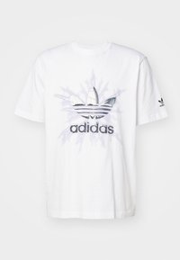 Bílý bavlněný tričko s velkým šedým a černým potiskem loga adidas. Krátké rukávy a kulatý výstřih. Měkká textura s volným střihem.