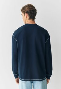 Granatowa, długosleeve bluza z okrągłym dekoltem, z kontrastowymi przeszyciami i luźnym krojem. Materiał wydaje się miękki i gładki.