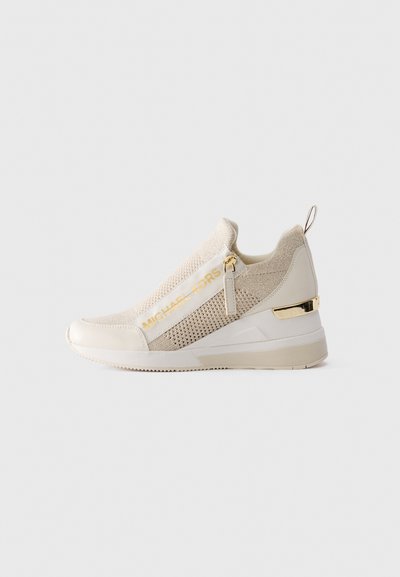 Baskets slip-on beige et crème en tissu en maille, avec fermeture éclair dorée, marque Michael Kors et accent doré sur la semelle compensée.