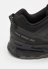 Black hiking shoe with textured mesh upper, cushioned collar, and rubber sole. Features brand marking and reinforced heel for stability.