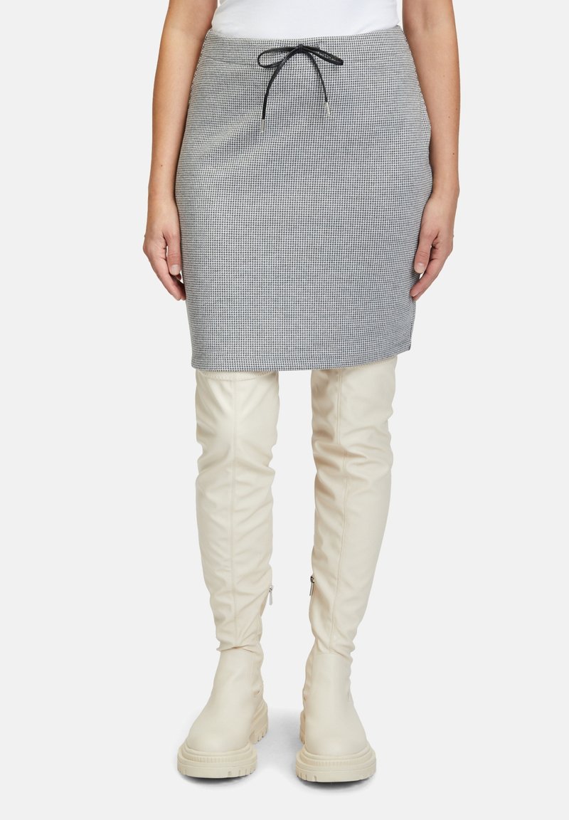 Szara spódnica w kratkę z elastycznym pasem, zestawiona z wysokimi, białymi botkami. Spódnica ma dopasowany krój i gładką teksturę.
