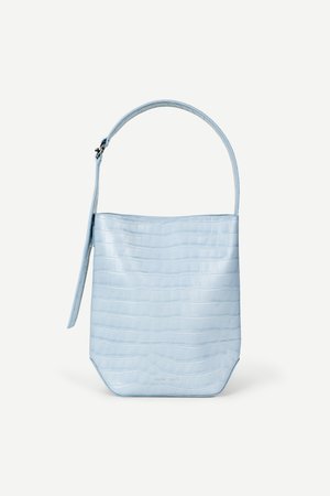 Sac à main bleu clair avec texture crocodile, forme rectangulaire, poignée unique en haut et une bandoulière latérale suspendue sur un fond blanc uni.