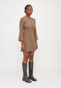Robe en tricot côtelé marron avec de longues manches en forme de cloche, associée à des bottes grises jusqu'au genou avec des boucles et un design à bout rond.
