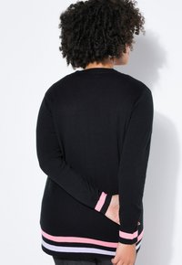 Schwarzer Pullover mit langen Ärmeln und gerippter Struktur. Saum und Bündchen sind mit rosa, lavendelfarbenen und weißen Streifen akzentuiert. Rückansicht gezeigt.