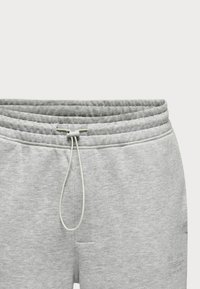 Pantalones de chándal grises hechos de una tela suave. Presentan una cintura elástica con cordón y un bolsillo frontal. Textura simple y suave.