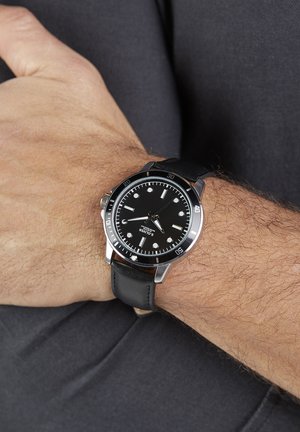 Schwarze Taucheruhr mit einem Gehäuse aus Edelstahl. Verfügt über ein schwarzes Zifferblatt, weiße Stundenmarkierungen und ein schwarzes Lederarmband. Mit geriffeltem Kronendetail.