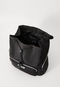 Black fabric backpack with a drawstring top, zippered front pocket, and silver hardware accents. Smooth texture, minimalist design.