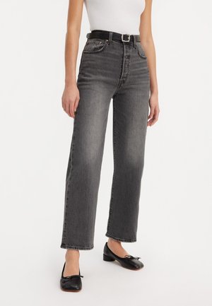 High-waisted, straight-leg black jeans in faded, textured fabric; paired with a black belt and black flats.