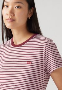 Crvena i bijela prugaasta majica s okruglim izrezom i kratkim rukavima. Ima mali crveni Levi's logo na prsima. Mekani pamučni materijal.