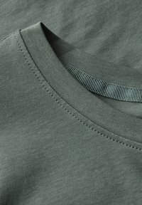 Närbild av en mjuk, grön T-shirtkrage med s�ömnadsdetaljer och en slät yta, som framhäver dess avslappnade stil.
