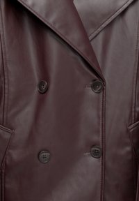 Cappotto doppiopetto in pelle bordeaux con ampi rever, bottoni neri e tasche laterali con una texture liscia.
