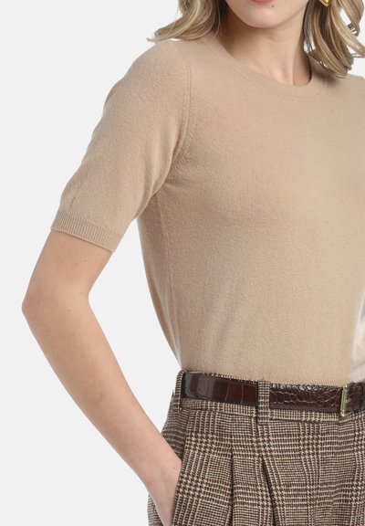 Beige īsām piedurknēm džemperis izgatavots no mīksta materiāla, ar vienkāršu apaļu kakla izgriezumu, kombinēts ar teksturētām brūnām svītrainām biksēm un spīdīgu brūnu jostu.