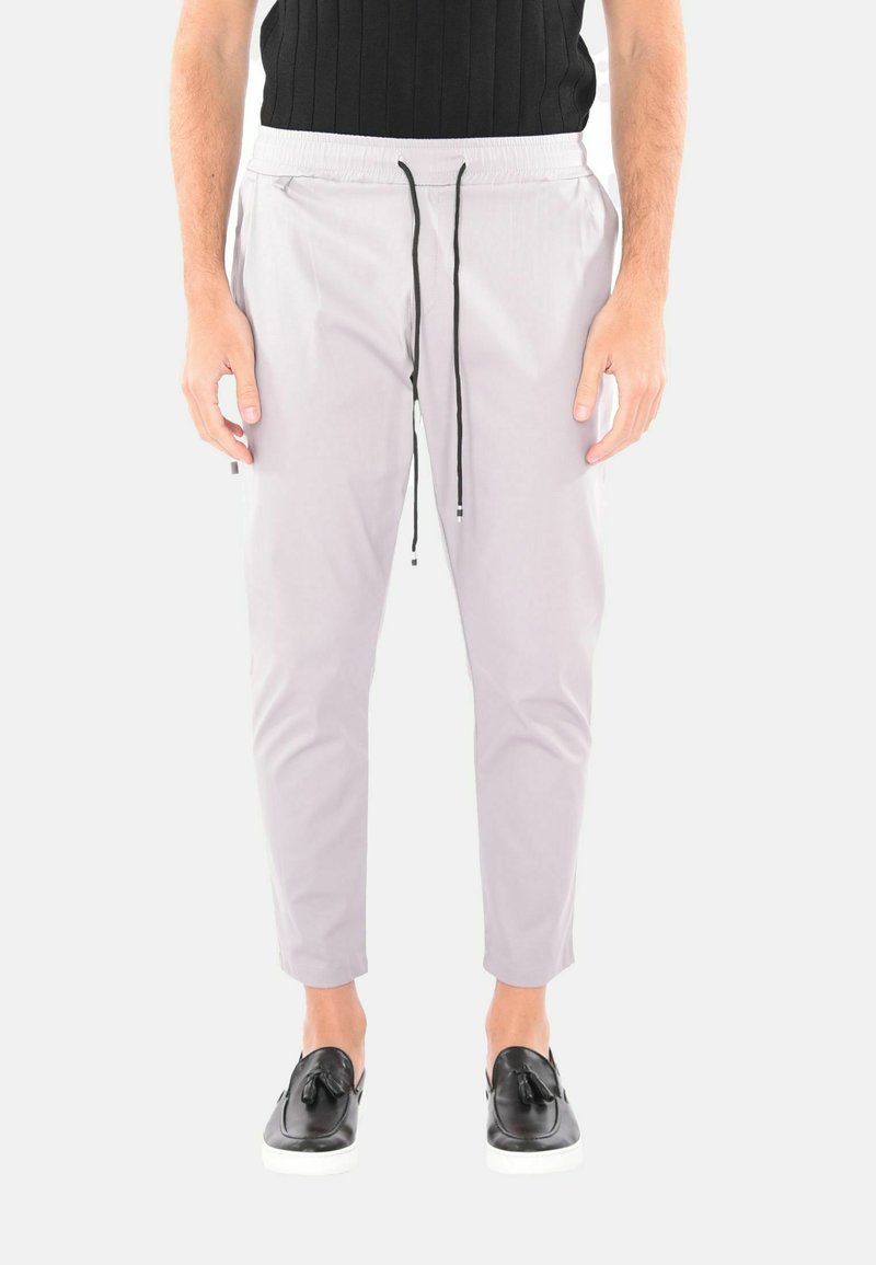 Pantaloni jogger grigi chiari con vita elasticizzata, coulisse e gamba affusolata, abbinati a scarpe nere slip-on con un dettaglio a fiocco.