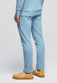 Lichtblauwe sweatpants met een gladde textuur en een elastische tailleband, gecombineerd met gele retro-sneakers met witte veters en groene accenten.
