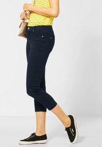 Pantalones cortos en azul marino de tela lisa con bolsillos frontales, herrajes en tono plateado y un corte relajado, combinados con zapatos negros de cordones.