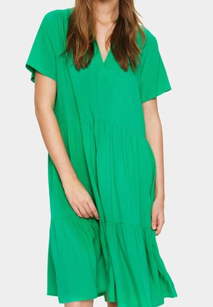 Grøn kjole med korte ærmer og V-udskæring, der har et lagdelt design og blødt stof, udviser en løs pasform og en mid-længde kant.