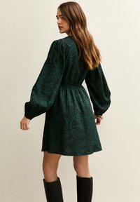 Groene jurk met zwart luipaardprint, getailleerde taille, lange pofmouwen en een uitlopende rok. Gemaakt van een glad stof, met een eenvoudig ontwerp.