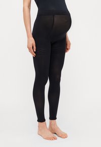 Juodos nėščiosios legging'os su lygia tekstūra ir aukšta juosmeniu, su subtiliais bangų raštais šonuose. Kulko ilgio dizainas.