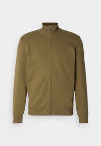 Alyvuogių žalios spalvos užtrauktuku užsegama striukė, pagaminta iš minkštos medžiagos, su aukštu apykakliu, pūkuotomis rankovėmis ir logotipo pleistru kairėje rankovėje.