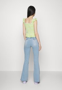 Top crop rufado verde e branco de padrão xadrez, com costas quadradas, combinado com jeans flare azul claro e sapatos de plataforma roxos.