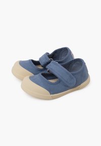 Zapatos Mary Jane de lona azul con una correa de Velcro, suelas de goma, costuras expuestas y diseño de punta redondeada. Suela beige texturizada.