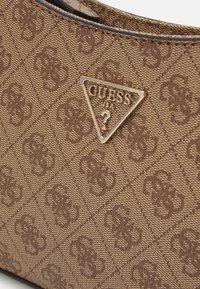 Sac à main marron texturé avec un motif de logo répété et un emblème triangulaire doré Guess USA avec un point d'interrogation.
