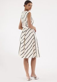 Sukienka bez rękawów w kolorze kremowym z czarnymi ukośnymi paskami, rozkloszowanym dołem i dopasowaną talią. Gładki materiał i akcent w postaci związanej talii.