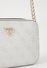 Weiße strukturierte Handtasche mit goldenem Guess-Logo, ausgestattet mit einem charakteristischen Muster, glatten Kanten und einem Kettenriemen zum Tragen.