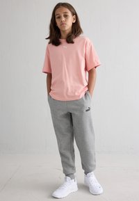 Ροζ βαμβακερό μπλουζάκι με κοντά μανίκια, συνδυασμένο με γκρίζες φόρμες που φέρουν μαύρο λογότυπο. Άσπρα αθλητικά παπούτσια ολοκληρώνουν το σύνολο.