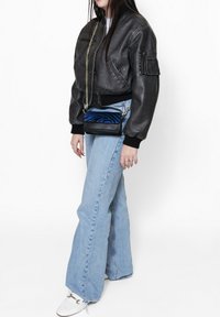 Giubbotto bomber in pelle nera con polsini a coste, jeans a zampa d'elefante blu chiaro e una piccola borsa a tracolla con strisce a zebra blu.