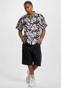 Camiseta de manga corta negra con un patrón floral blanco y rosa. Combinada con pantalones cortos negros y zapatillas blancas, creando un look informal.