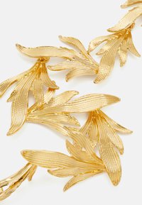 Guldtonet metalbroche med teksturerede, bladformede elementer med ribbede detaljer, arrangeret i et overlappende mønster.