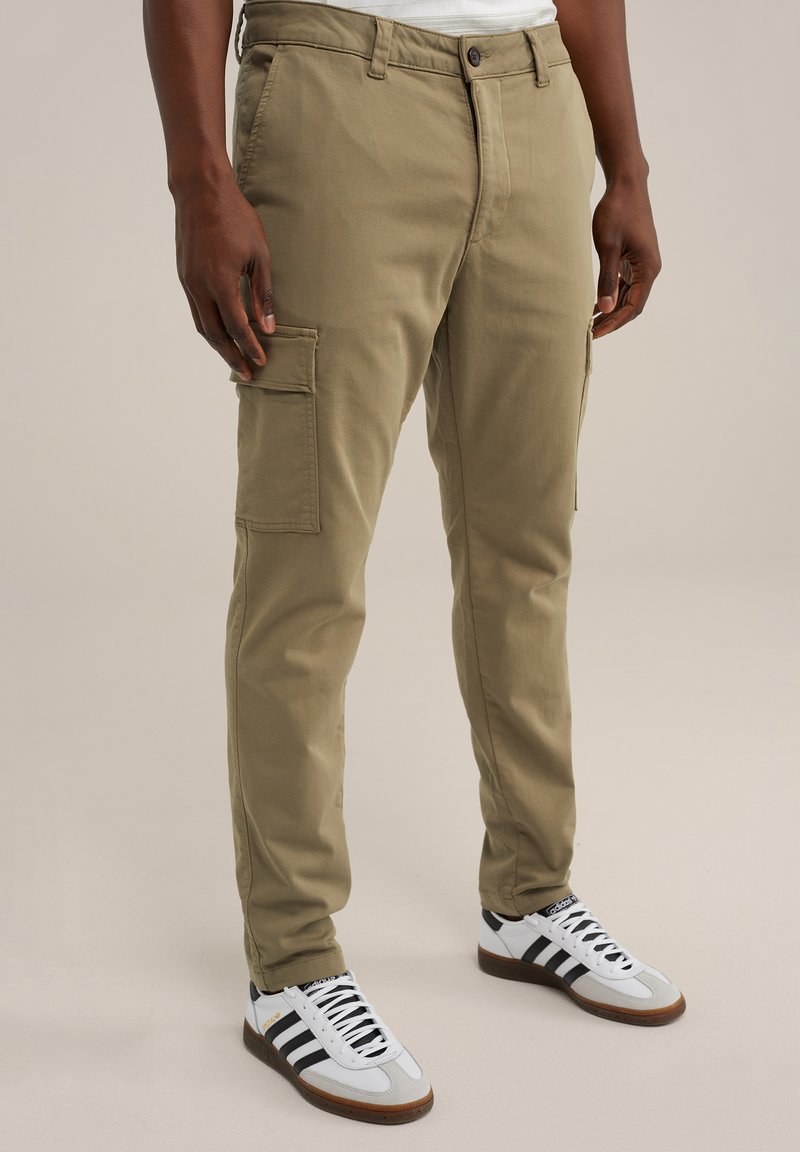 Khaki színű, slim fit cargo nadrág, oldalsó zsebekkel, övbújtatókkal és cipzárral. Fehér sportcipővel viselve, fekete csíkokkal.