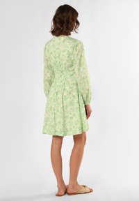 Green floral patterned dress, cinched waist, long sleeves, knee-length, lightweight fabric, relaxed fit, matched with beige sandals.