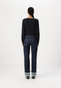 Vaqueros de lavado azul oscuro, con pierna recta y puños doblados distintivos con la palabra "BLANCHE" impresa en ellos. Combinados con un suéter negro.
