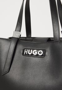 Svarte skinnveske med sølv "HUGO"-logo, glatt tekstur, doble håndtak og rektangulær form. Utsmykket med metallbeslag.
