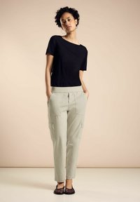 Svart kortärmad topp med en lätt off-shoulder-design, kombinerad med ljuskrämfärgad cargobyxor med sidofickor. Texturerade svarta platta skor.