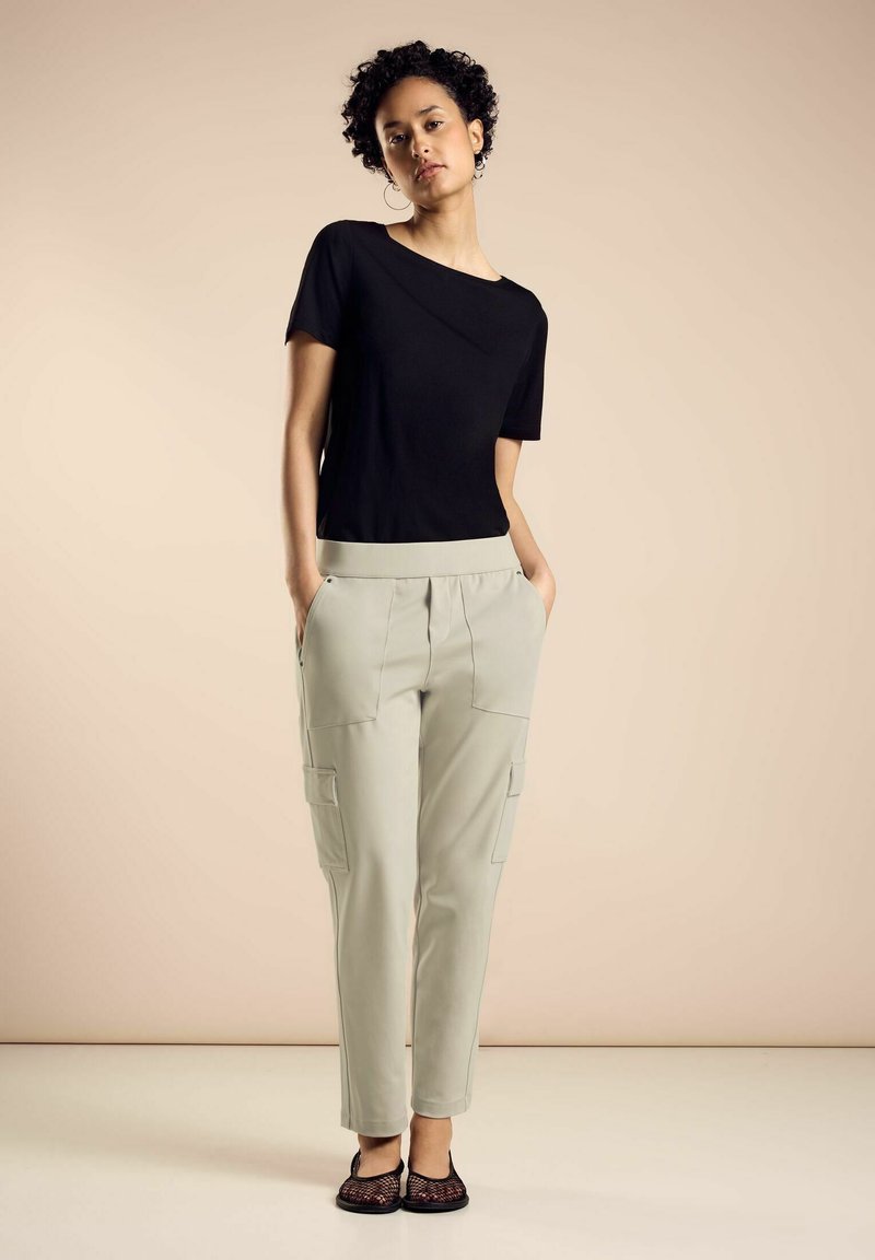 Svart kortärmad topp med en lätt off-shoulder-design, kombinerad med ljuskrämfärgad cargobyxor med sidofickor. Texturerade svarta platta skor.